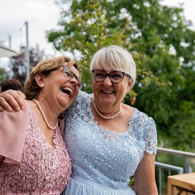 Zwei Gäste lachen Arm in Arm beim Apéro